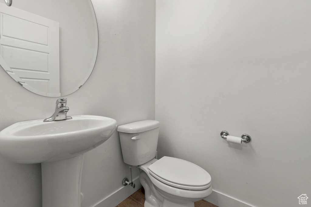 Half bath featuring baseboards, toilet, a sink, and wood finished floors