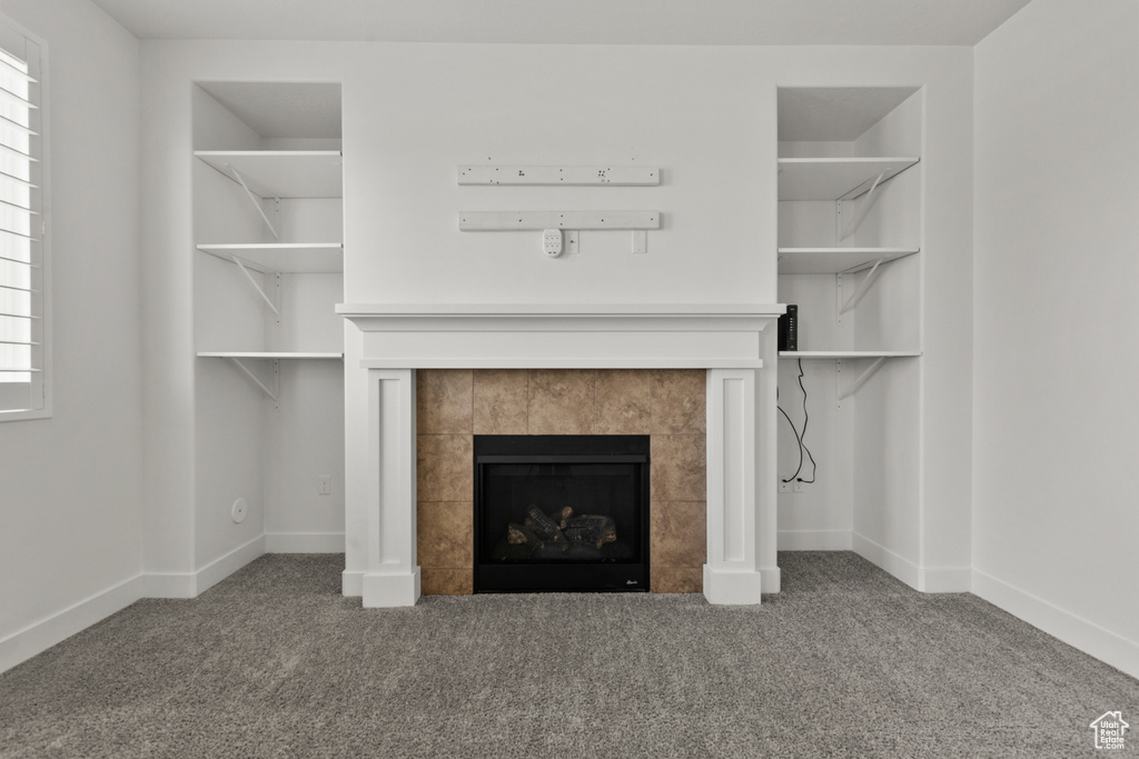 Unfurnished living room featuring a tiled fireplace, carpet flooring, and baseboards