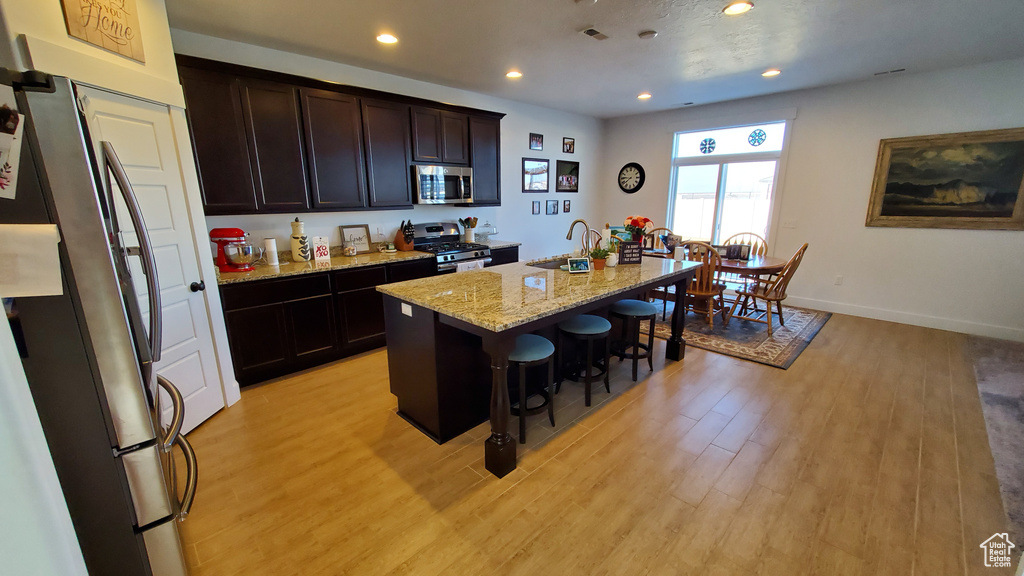 Kitchen featuring appliances with stainless steel finishes, light wood-style floors, a kitchen bar, an island with sink, and recessed lighting