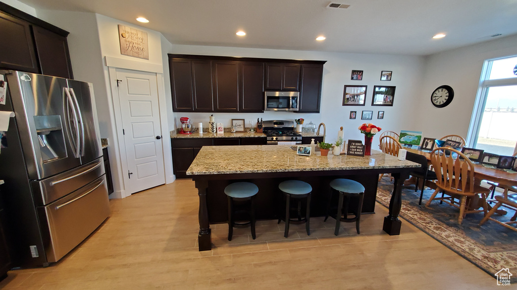 Kitchen featuring stainless steel appliances, a breakfast bar area, light stone countertops, dark brown cabinets, and recessed lighting