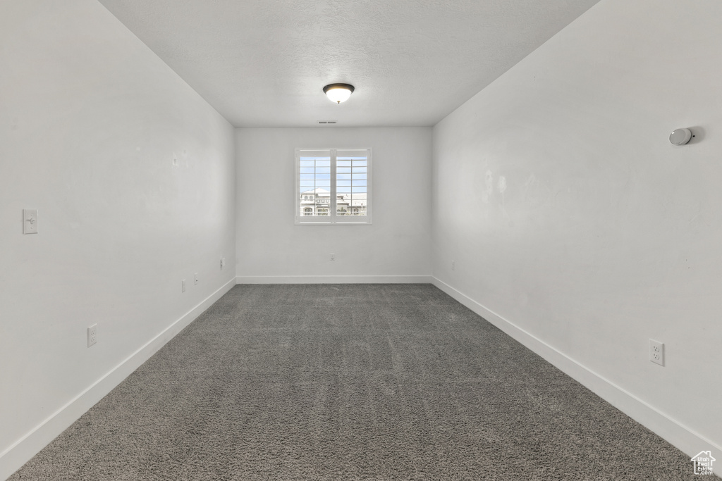 Unfurnished room featuring dark colored carpet and baseboards