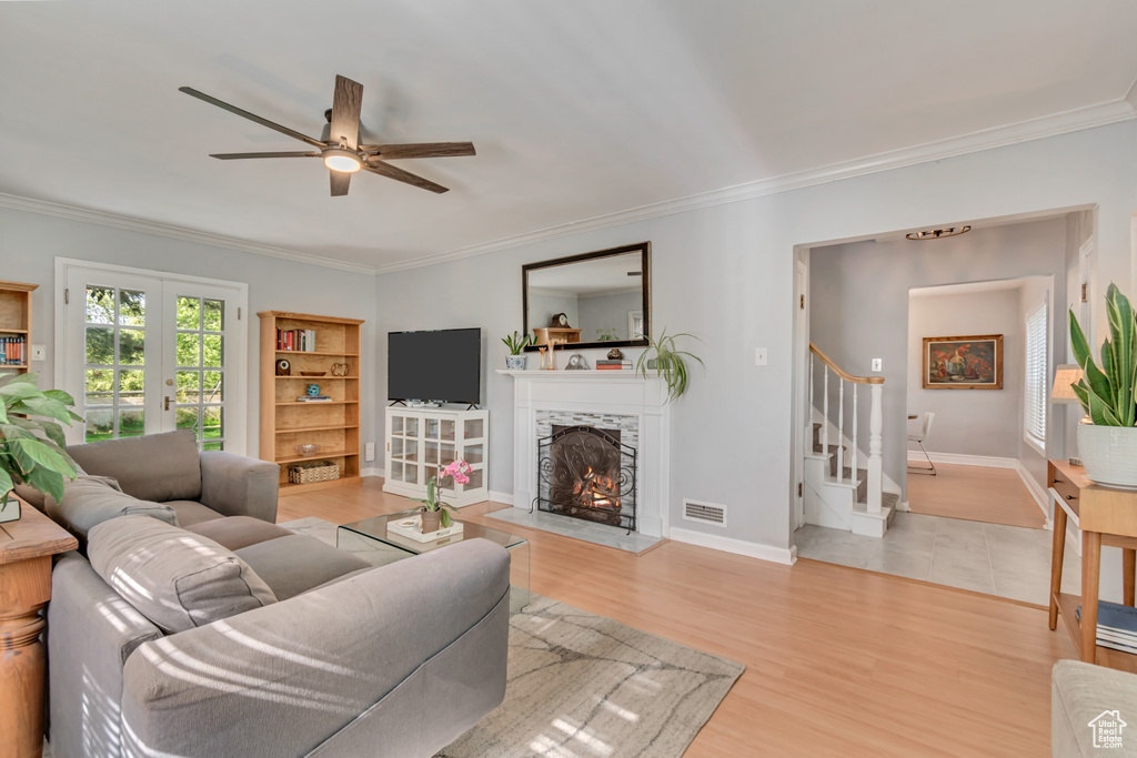 Living area featuring stairs, ornamental molding, ceiling fan, a lit fireplace, and light wood-style floors
