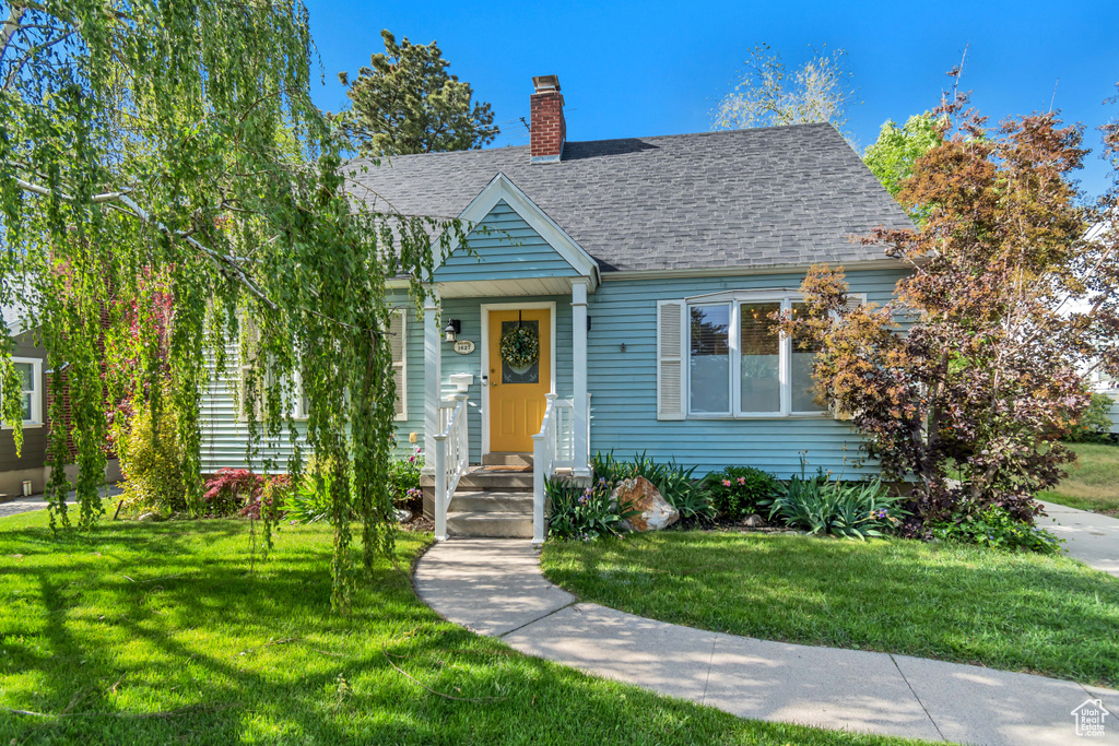 View of front facade with a chimney, a front yard, and a shingled roof
