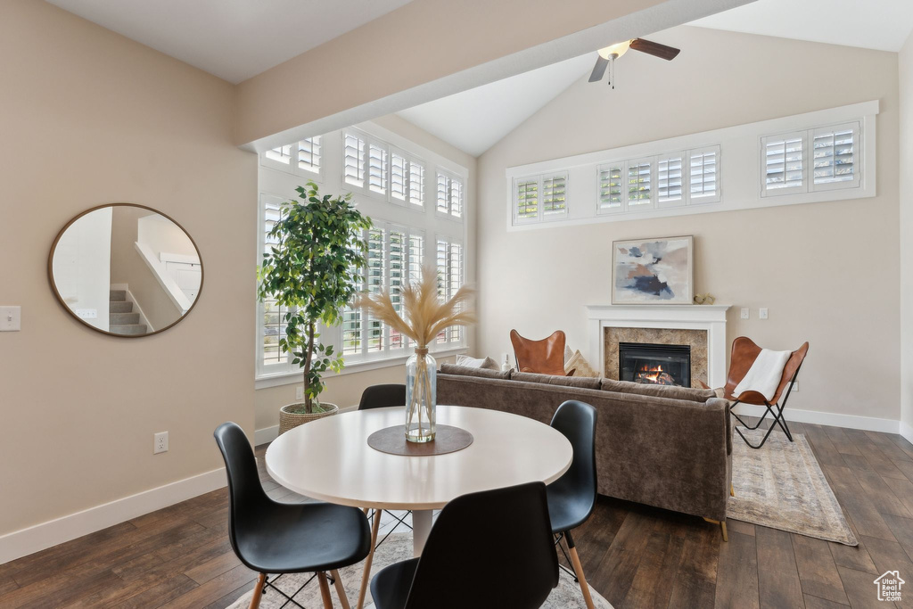 Dining area featuring ceiling fan, a glass covered fireplace, dark wood-type flooring, high vaulted ceiling, and baseboards