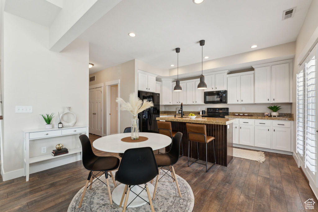 Kitchen with black appliances, dark wood-style flooring, white cabinetry, a center island with sink, and decorative light fixtures