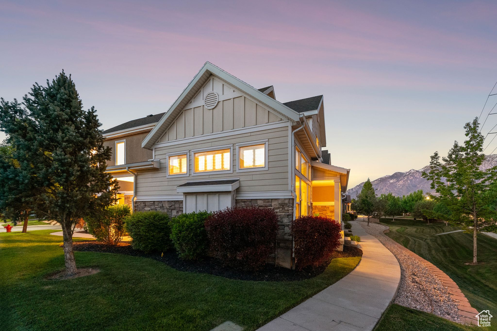 Rear view of property with board and batten siding, stone siding, a lawn, and a mountain view
