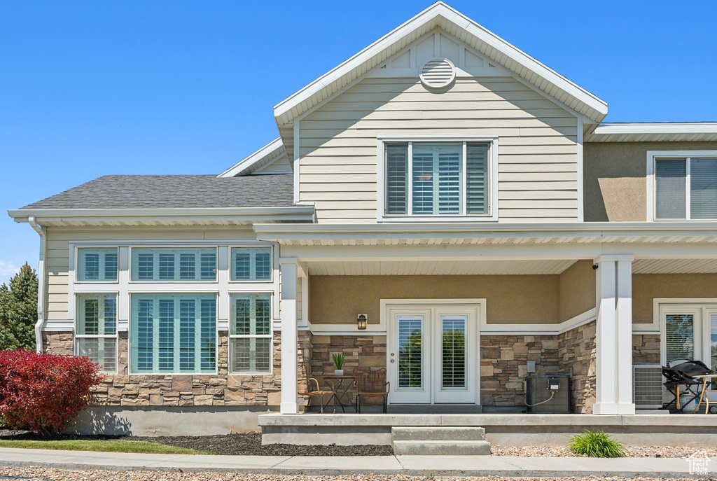 View of front of property with stone siding, a porch, and a shingled roof