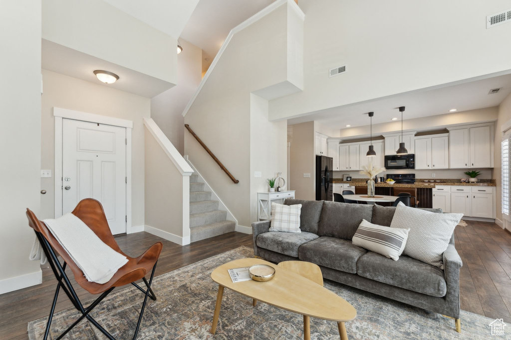 Living room with dark wood-style flooring, stairs, baseboards, high vaulted ceiling, and recessed lighting