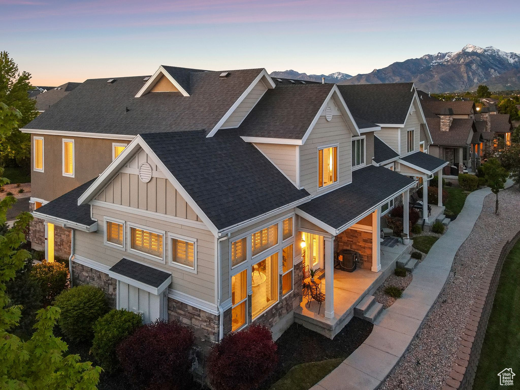 Back of house at dusk with stone siding, roof with shingles, board and batten siding, and a mountain view
