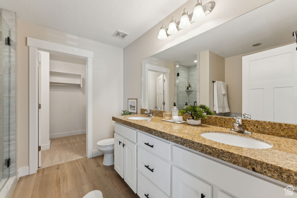 Full bath featuring a shower stall, double vanity, toilet, wood finished floors, and baseboards