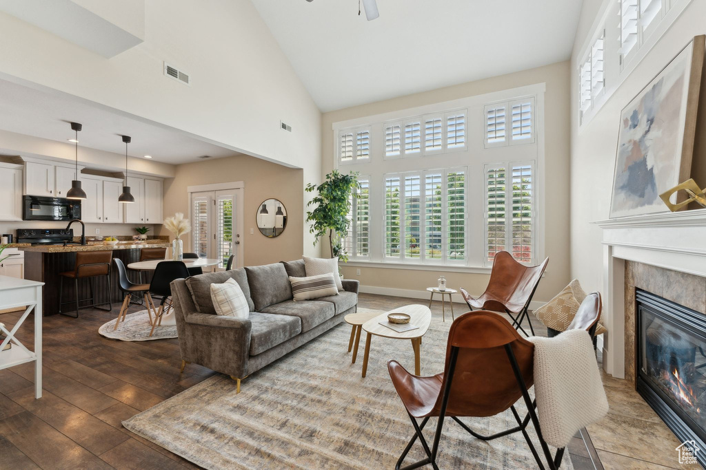 Living room featuring a fireplace, wood-type flooring, a high ceiling, and a ceiling fan