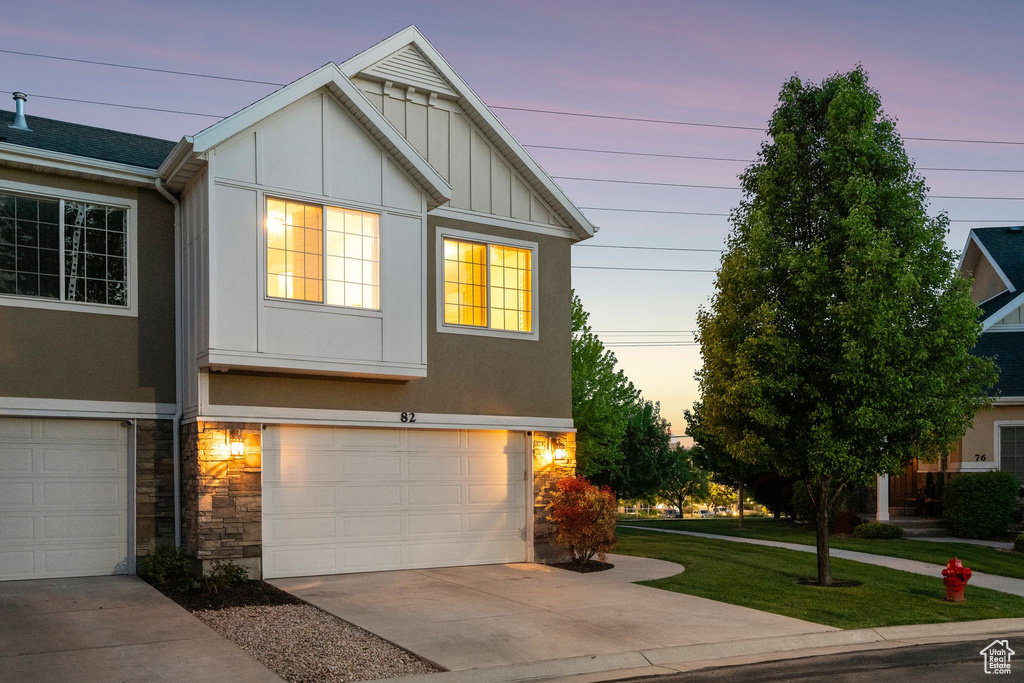 View of front of property with board and batten siding, a garage, driveway, stone siding, and a front lawn
