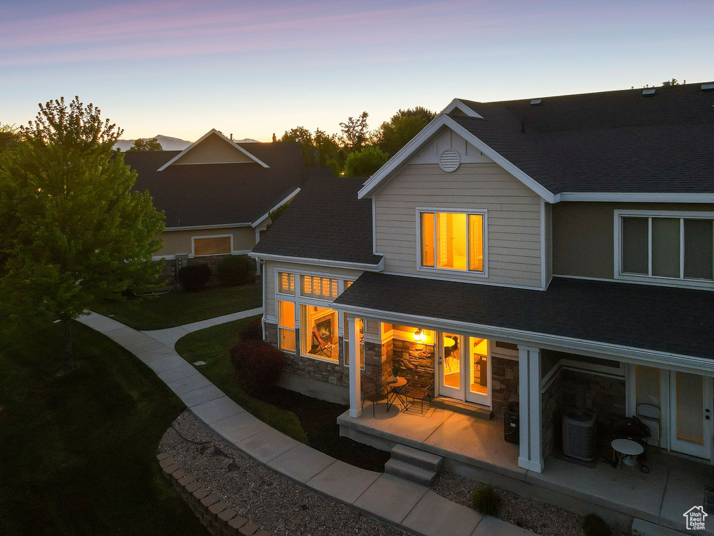 Rear view of house with a patio area, cooling unit, stone siding, and a shingled roof