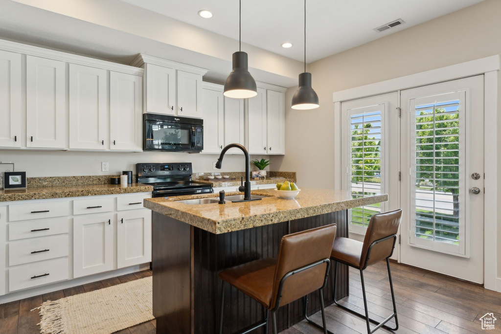 Kitchen featuring black appliances, a sink, white cabinets, a kitchen island with sink, and dark wood-type flooring