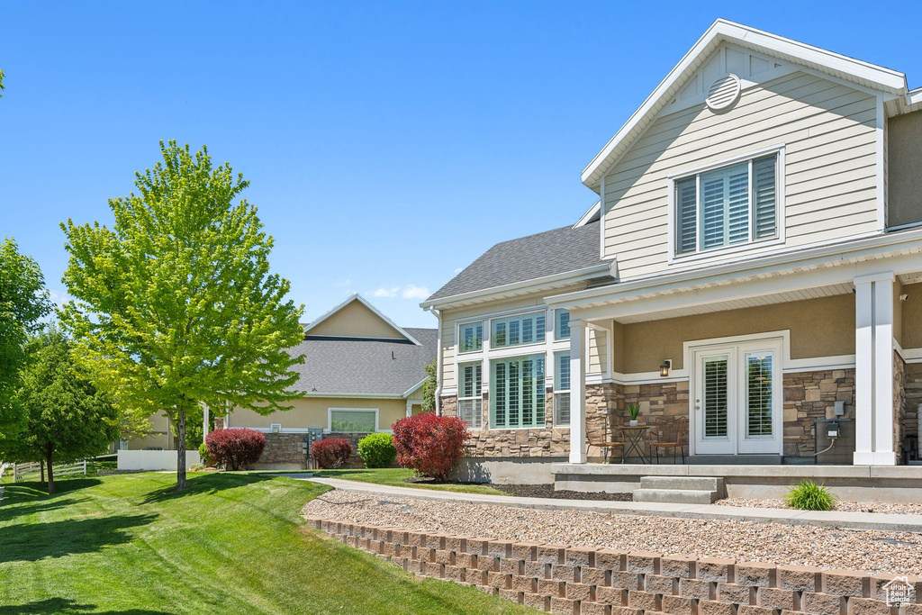 Rear view of property featuring stone siding, a lawn, french doors, and roof with shingles