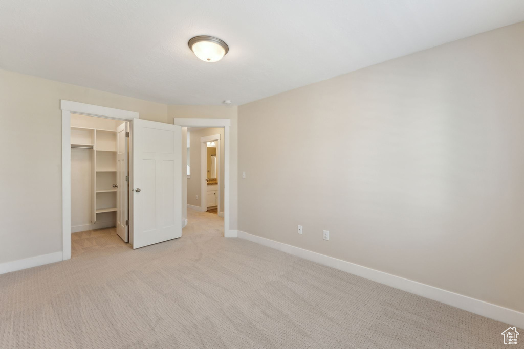 Unfurnished bedroom featuring light colored carpet, baseboards, a walk in closet, and a closet