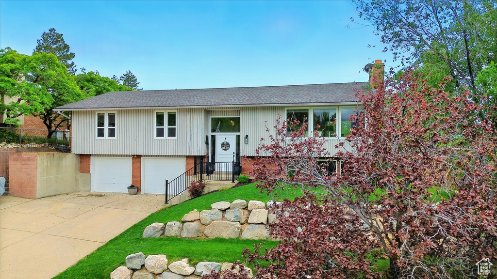 Bi-level home with an attached garage, concrete driveway, brick siding, a chimney, and a shingled roof