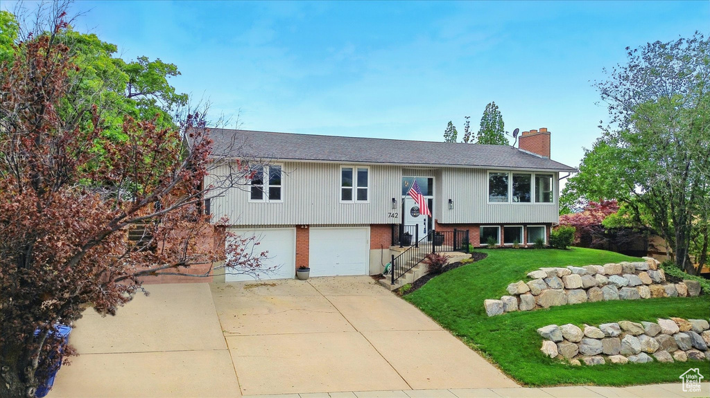 Split foyer home with a chimney, a front lawn, brick siding, driveway, and a garage