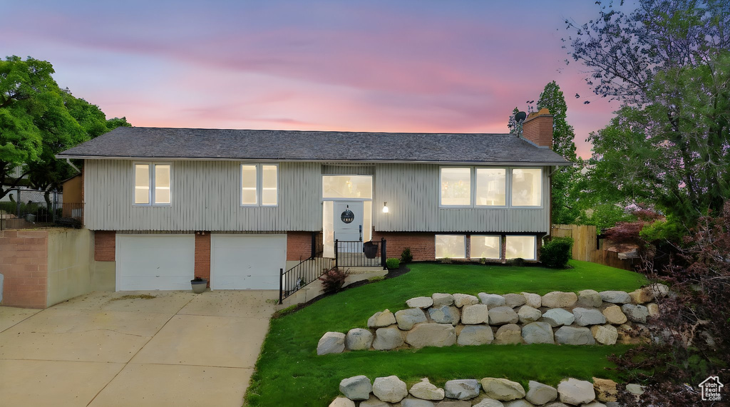 Bi-level home featuring brick siding, a chimney, an attached garage, concrete driveway, and roof with shingles