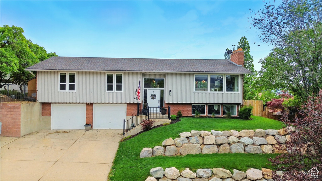 Split foyer home featuring a chimney, roof with shingles, concrete driveway, a garage, and brick siding