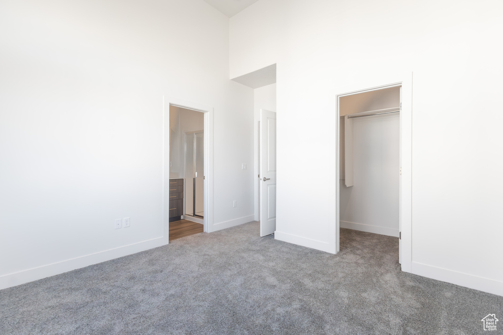 Unfurnished bedroom featuring a spacious closet, carpet flooring, a towering ceiling, baseboards, and a closet