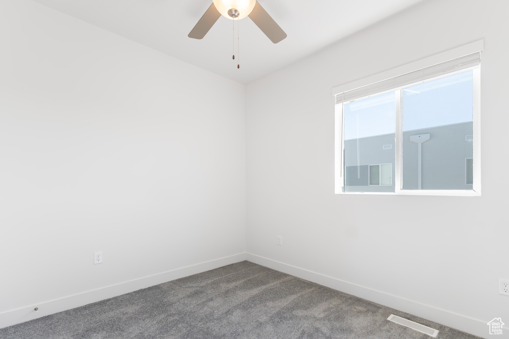 Carpeted spare room featuring ceiling fan and baseboards