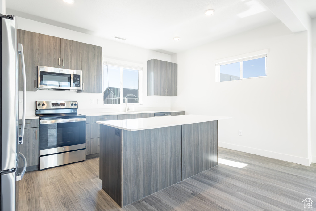 Kitchen featuring stainless steel appliances, light wood finished floors, light countertops, modern cabinets, and a center island