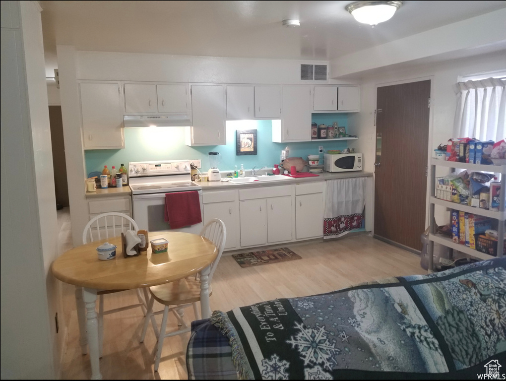 Kitchen with white appliances, a sink, light wood-style flooring, and white cabinets