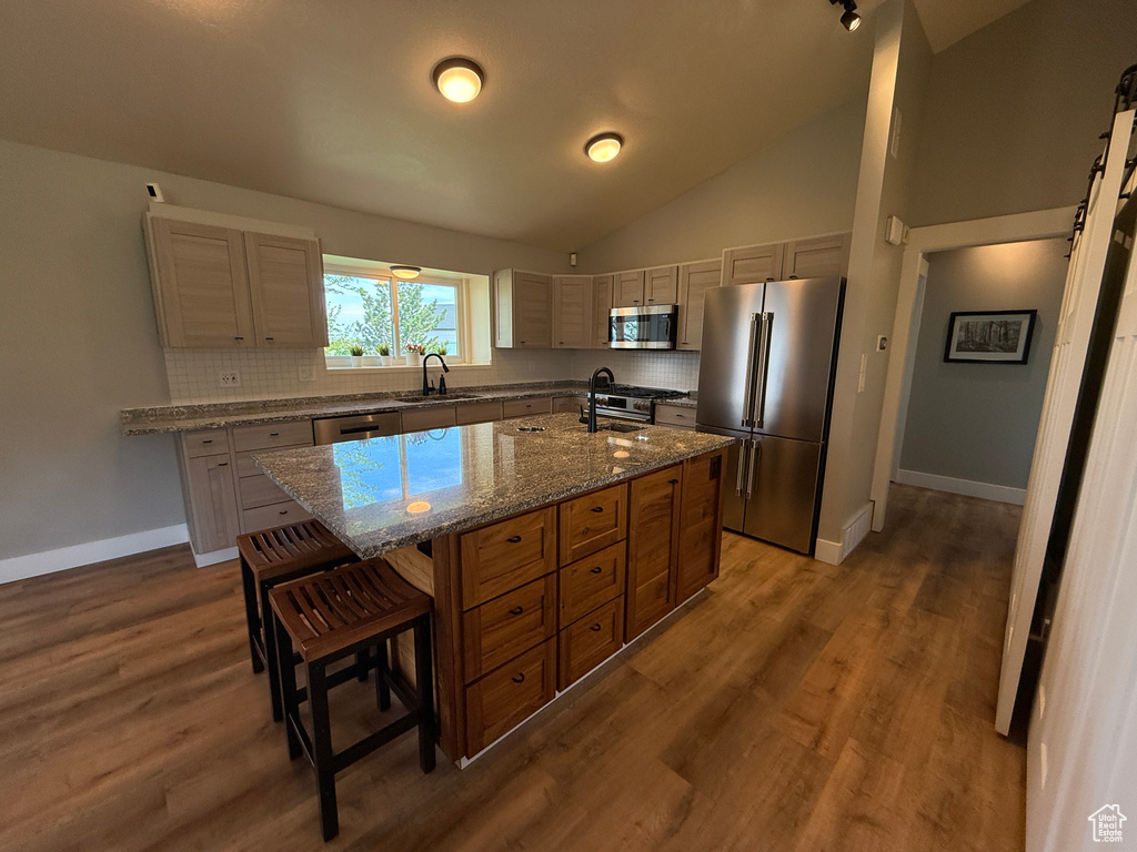 Kitchen featuring high end appliances, a sink, tasteful backsplash, a breakfast bar, and vaulted ceiling