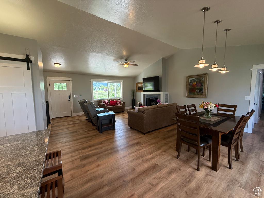 Dining space with ceiling fan, wood finished floors, a barn door, vaulted ceiling, and a fireplace