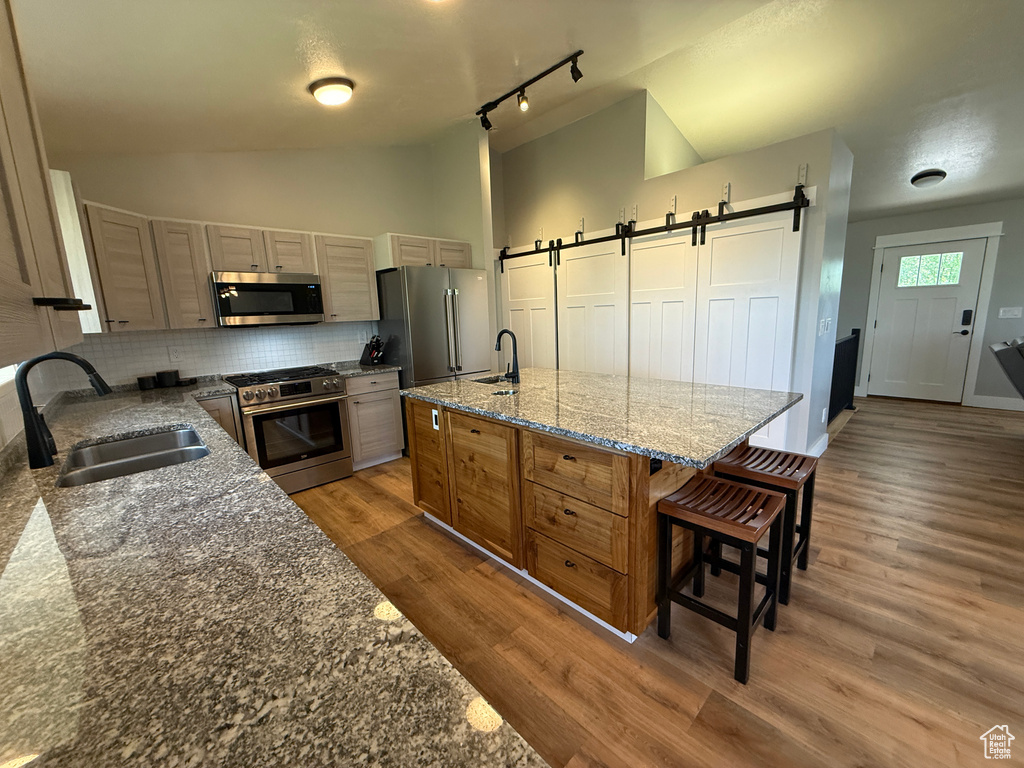Kitchen featuring stainless steel appliances, a sink, a barn door, decorative backsplash, and vaulted ceiling