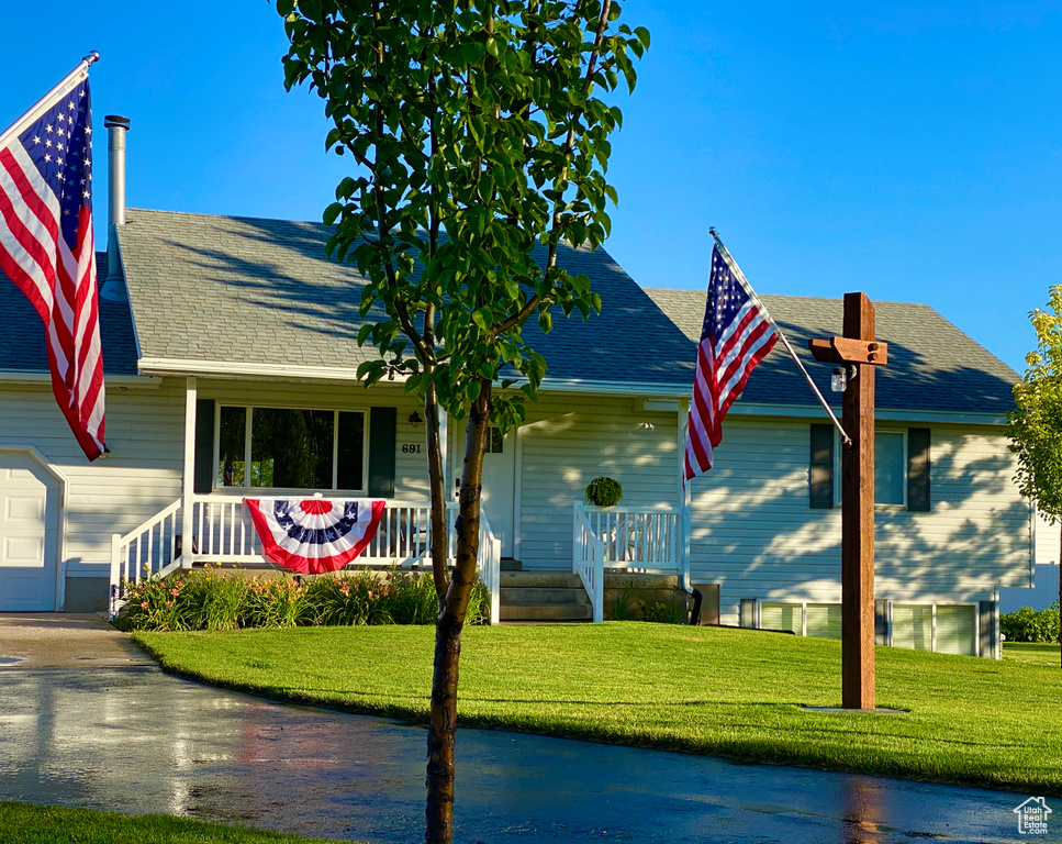 View of front of home with a porch, a shingled roof, a front yard, and driveway