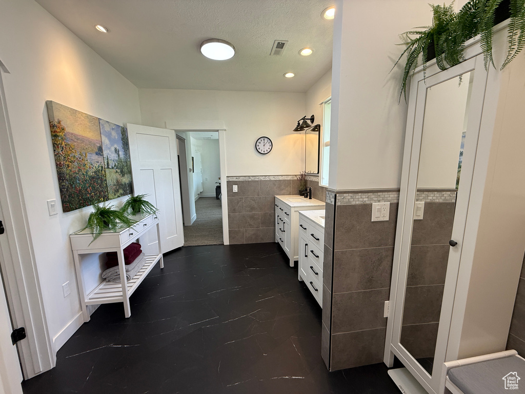 Bathroom featuring tile walls, wainscoting, vanity, and recessed lighting