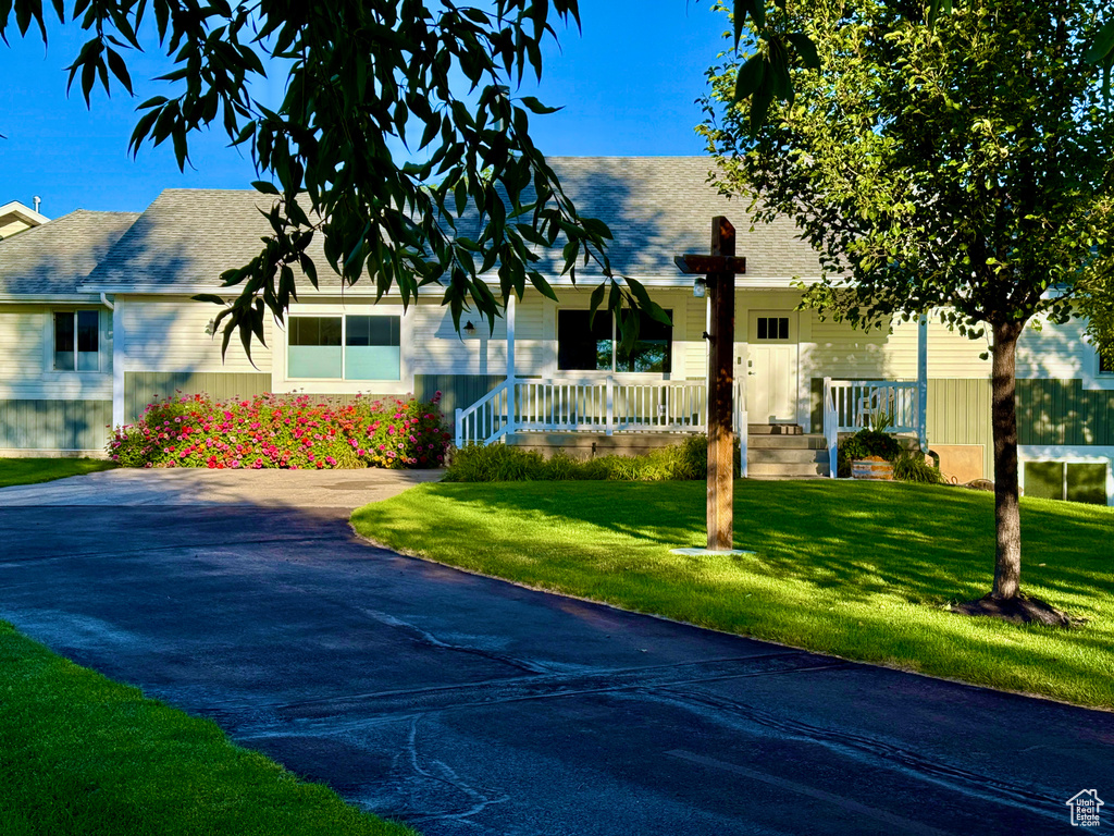 Ranch-style house featuring covered porch, roof with shingles, and a front lawn