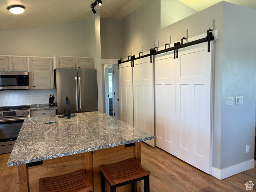 Kitchen with stainless steel appliances, a barn door, a sink, backsplash, and light wood-style floors