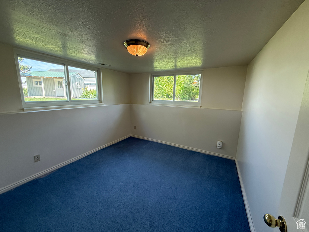Spare room featuring a textured ceiling, dark colored carpet, and baseboards
