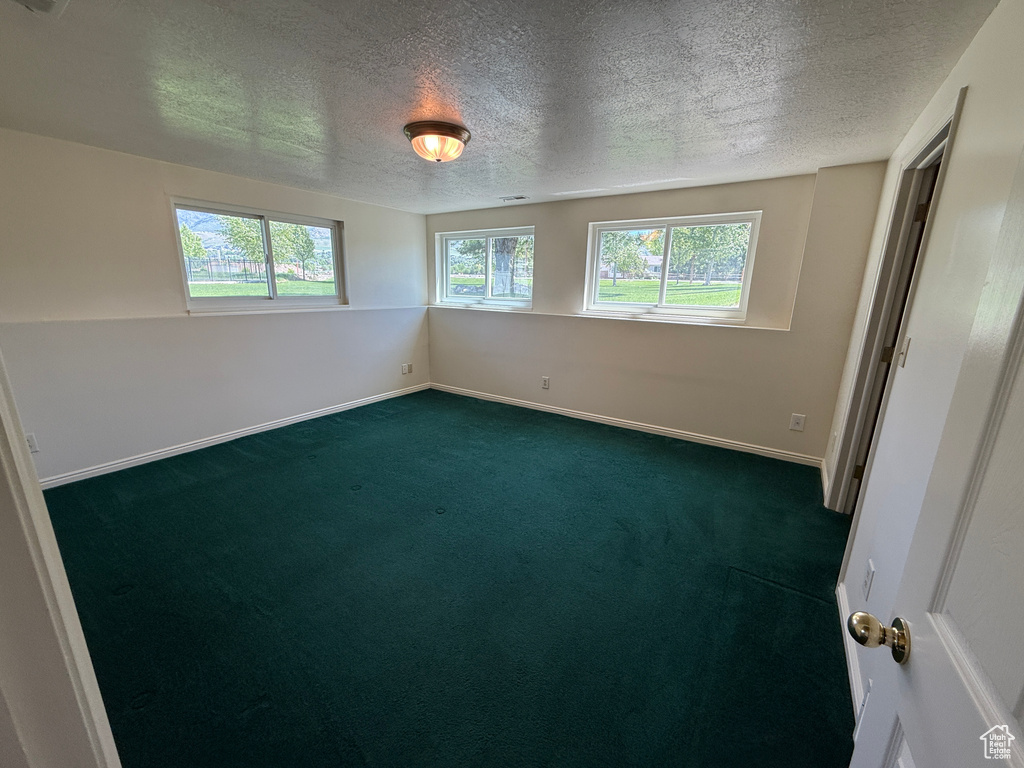 Empty room featuring dark colored carpet, a textured ceiling, and baseboards