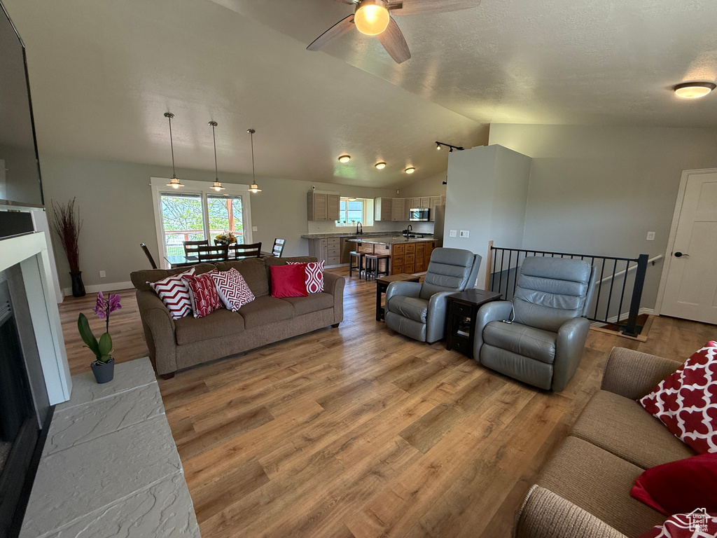 Living room featuring vaulted ceiling, ceiling fan, light wood-type flooring, baseboards, and a fireplace