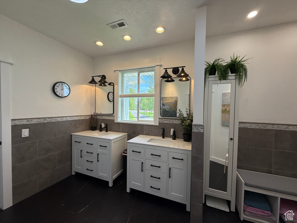 Full bath with tile walls, wainscoting, two vanities, tile patterned flooring, and recessed lighting