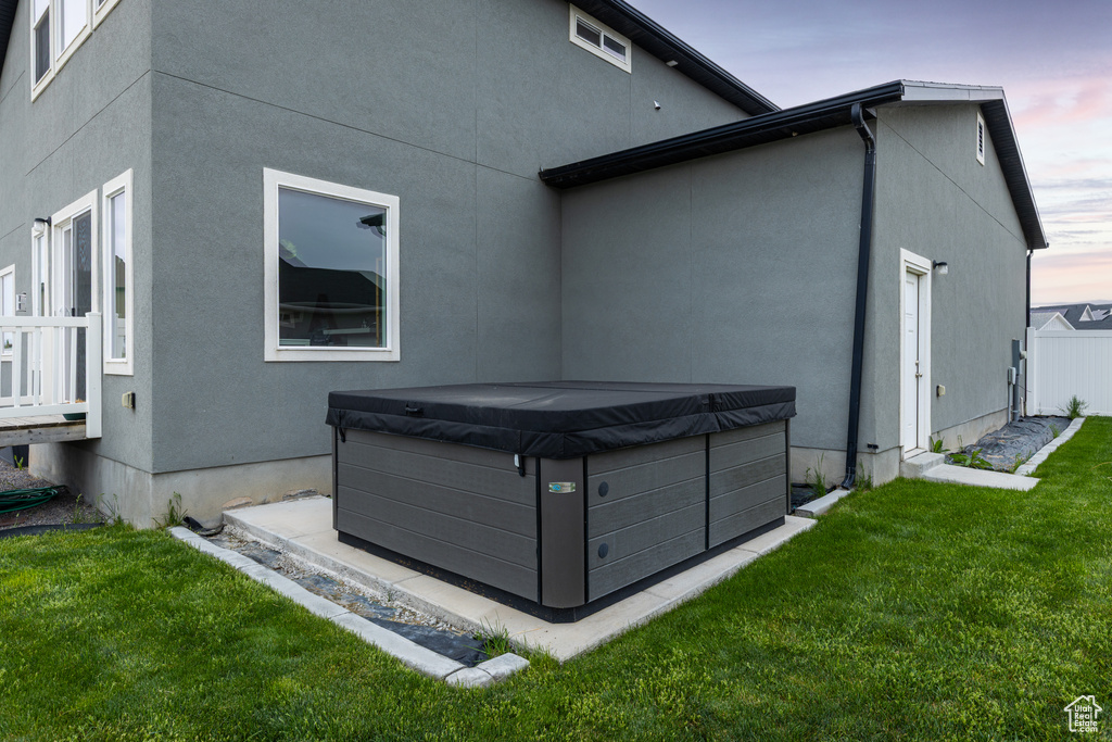 Rear view of house featuring a hot tub, a yard, and stucco siding
