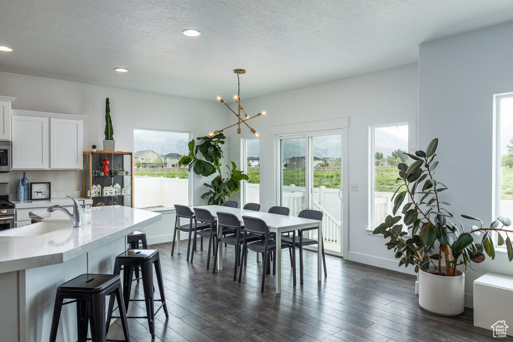 Dining space with plenty of natural light, a textured ceiling, a chandelier, dark wood-type flooring, and baseboards
