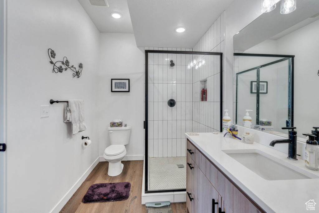 Bathroom with wood finished floors, a stall shower, toilet, baseboards, and vanity
