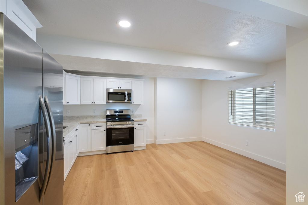 Kitchen featuring stainless steel appliances, baseboards, light wood-style floors, white cabinetry, and recessed lighting