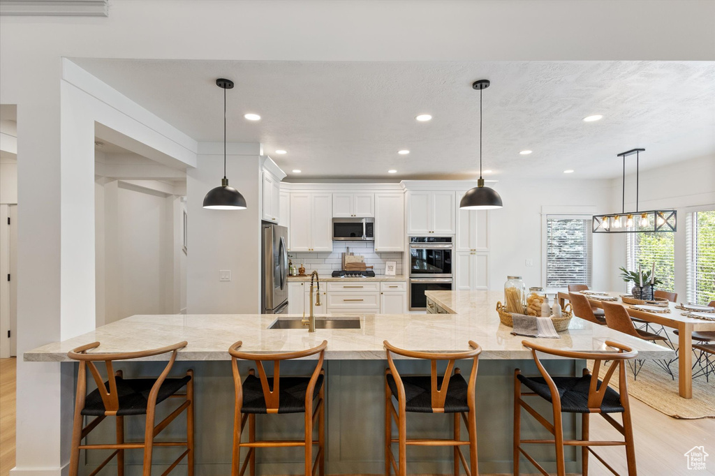 Kitchen featuring appliances with stainless steel finishes, a sink, light wood-type flooring, white cabinets, and backsplash