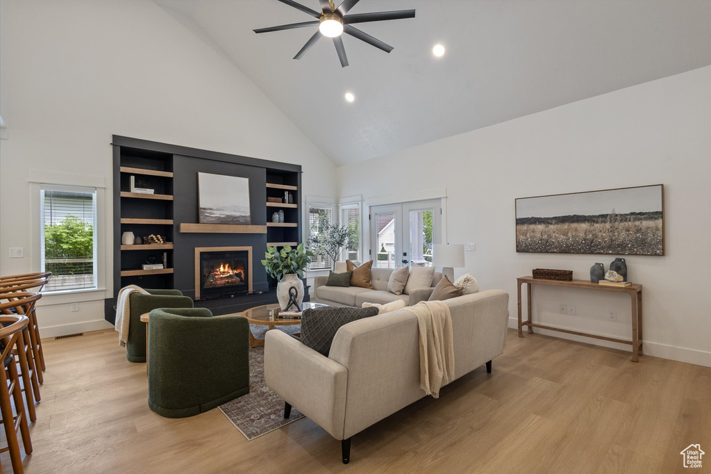 Living area featuring high vaulted ceiling, a ceiling fan, a glass covered fireplace, french doors, and light wood-style floors