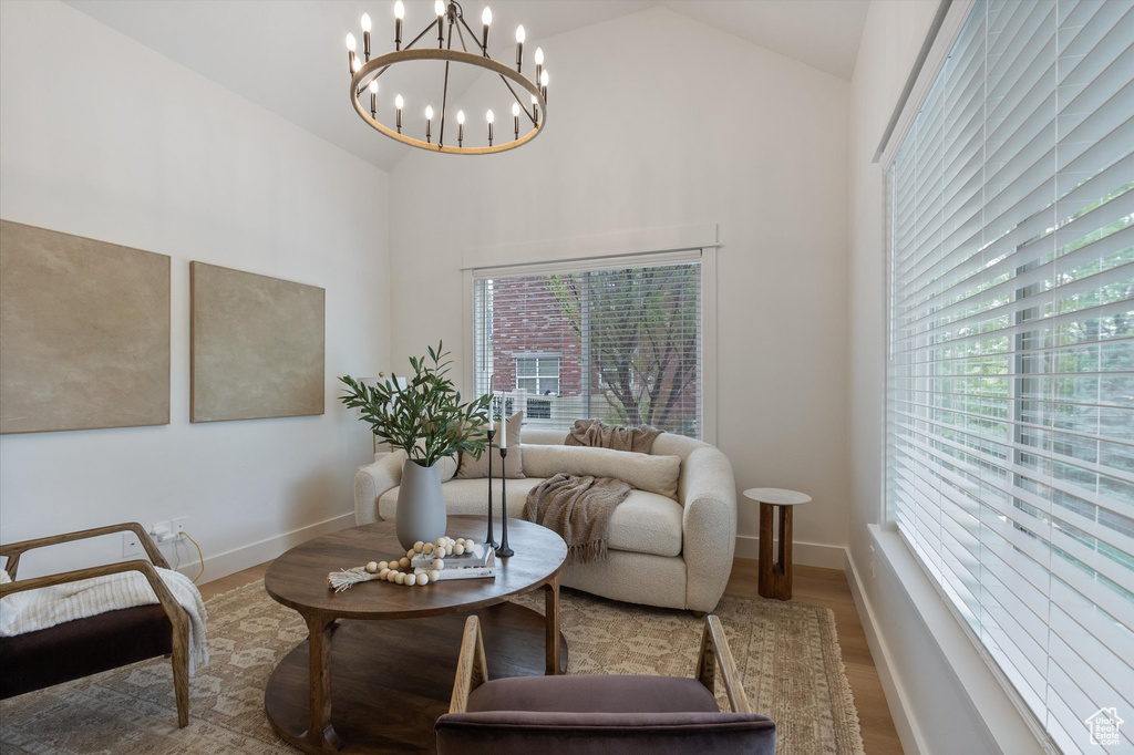 Living area with high vaulted ceiling, wood finished floors, a chandelier, healthy amount of natural light, and baseboards