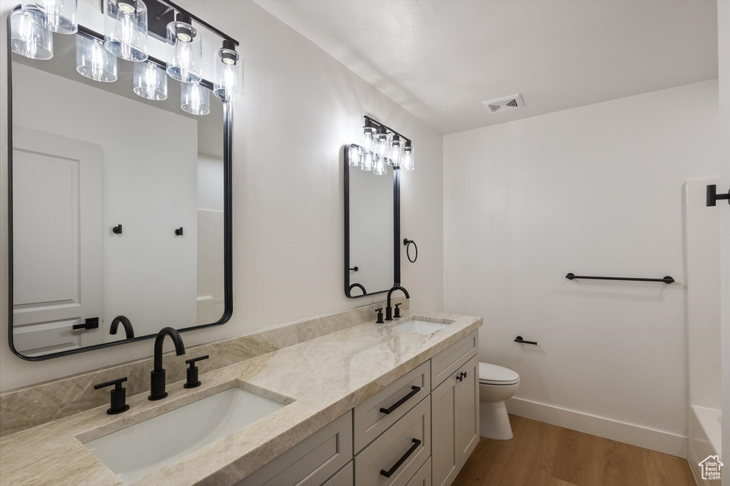 Full bath with toilet, wood finished floors, baseboards, and double vanity