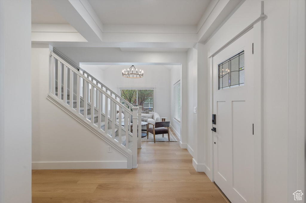 Foyer with light wood-type flooring, a chandelier, baseboards, and stairway