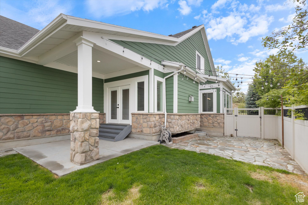 Back of house featuring a gate, french doors, stone siding, and a shingled roof