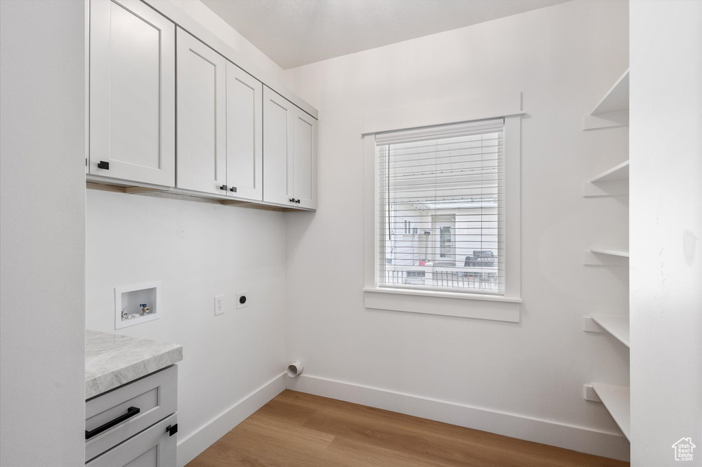 Clothes washing area with cabinet space, baseboards, hookup for a washing machine, and light wood-style flooring